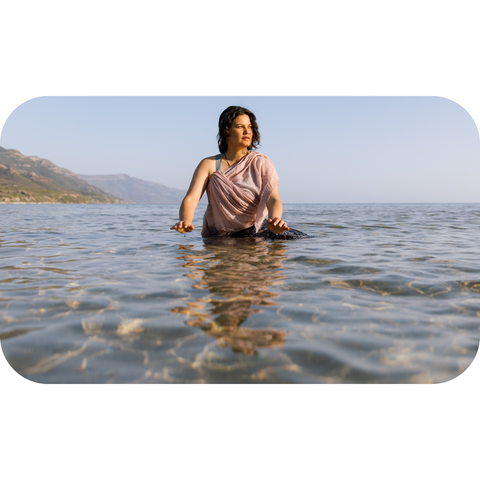 Woman sitting in the ocean with mountains in the background