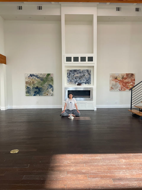 woman sitting clrosslegged on the wooden floor meditation with incense in front of her paintings in the back